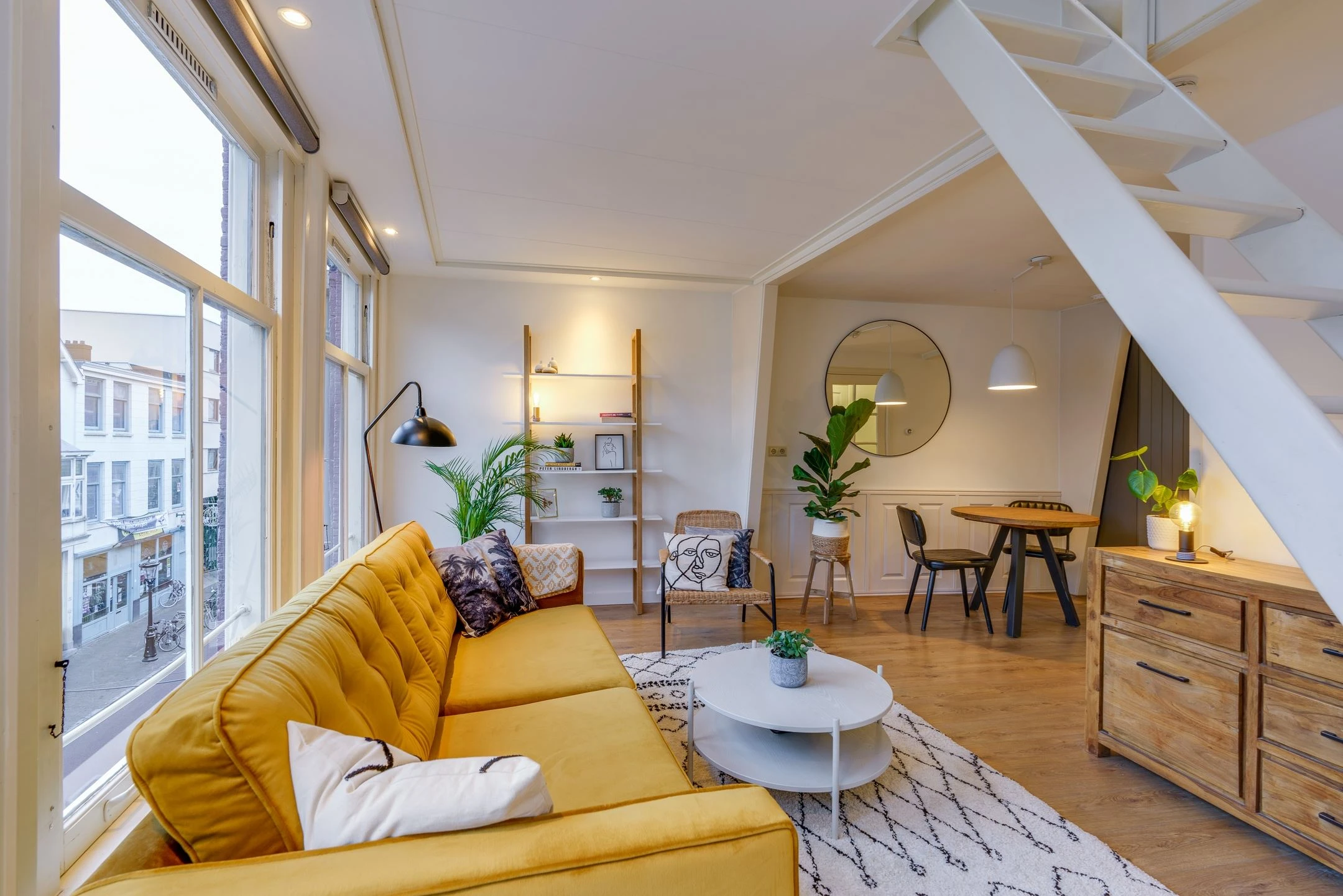 After: the same Airbnb living room with a mustard velvet sofa, cream Berber-style rug, and a styled ladder shelf