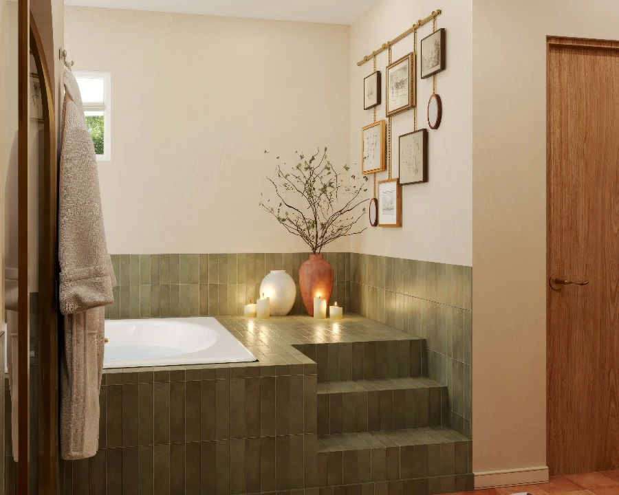 Green zellige tub surround and tiled steps below framed sketches hung from a brass rail, with candles