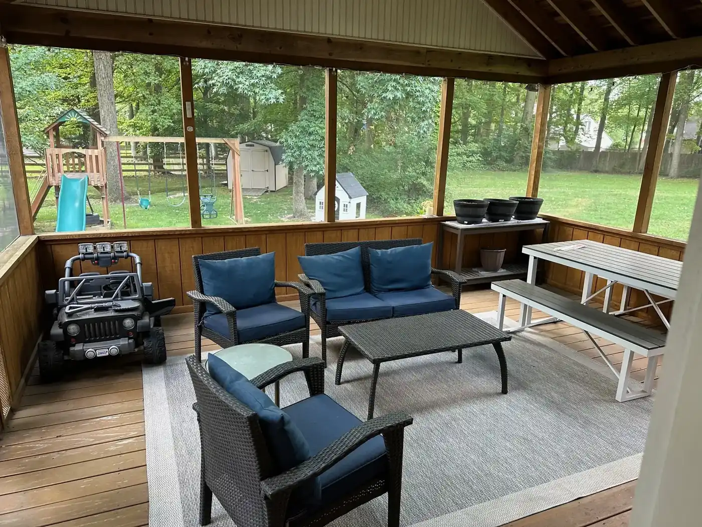 Before: screened porch with navy cushioned wicker seating, a picnic table and black planters on exposed deck boards