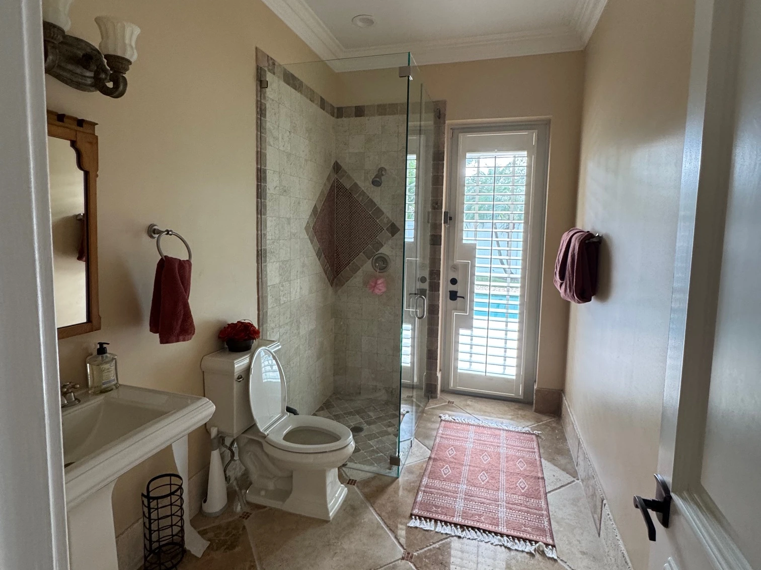 Before: beige bathroom with a diamond set travertine floor, a corner glass shower and a white pedestal sink