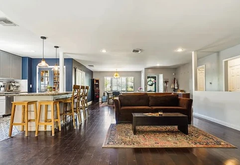 Open concept living room before with a brown leather sofa and dated kitchen and plain walls