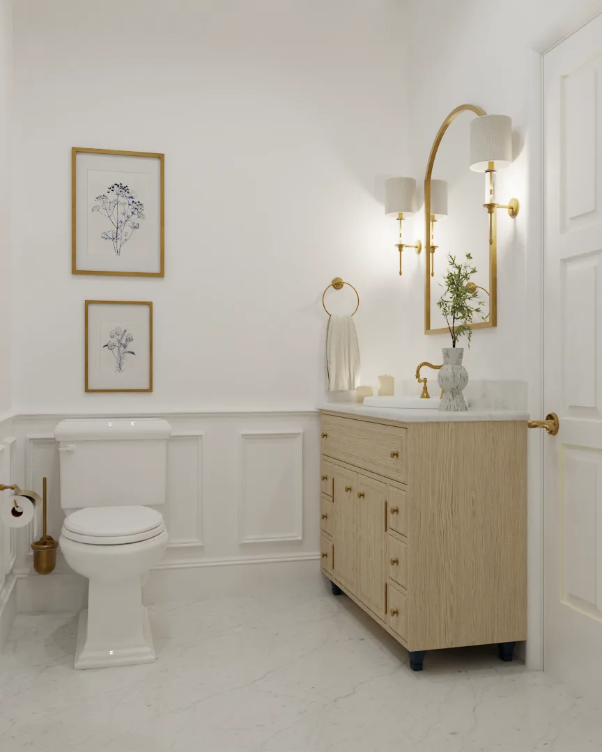 White bathroom with oak vanity, arched gold mirror, gold sconces, wainscoting panels, and botanical art prints