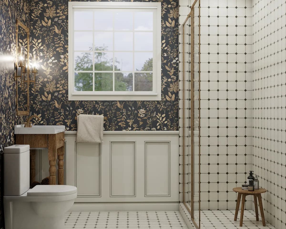 Compact bathroom with dark navy botanical wallpaper, cream wainscoting, oak vanity, brass shower frame, and white dot tile floor