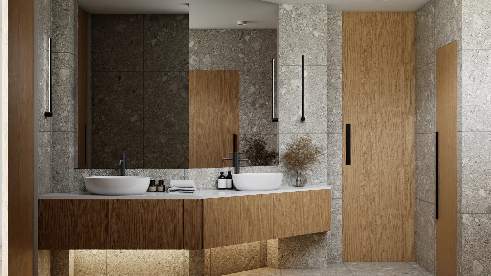 Wide view of double oak vanity, dual vessel sinks, and terrazzo tile walls with frameless shower door
