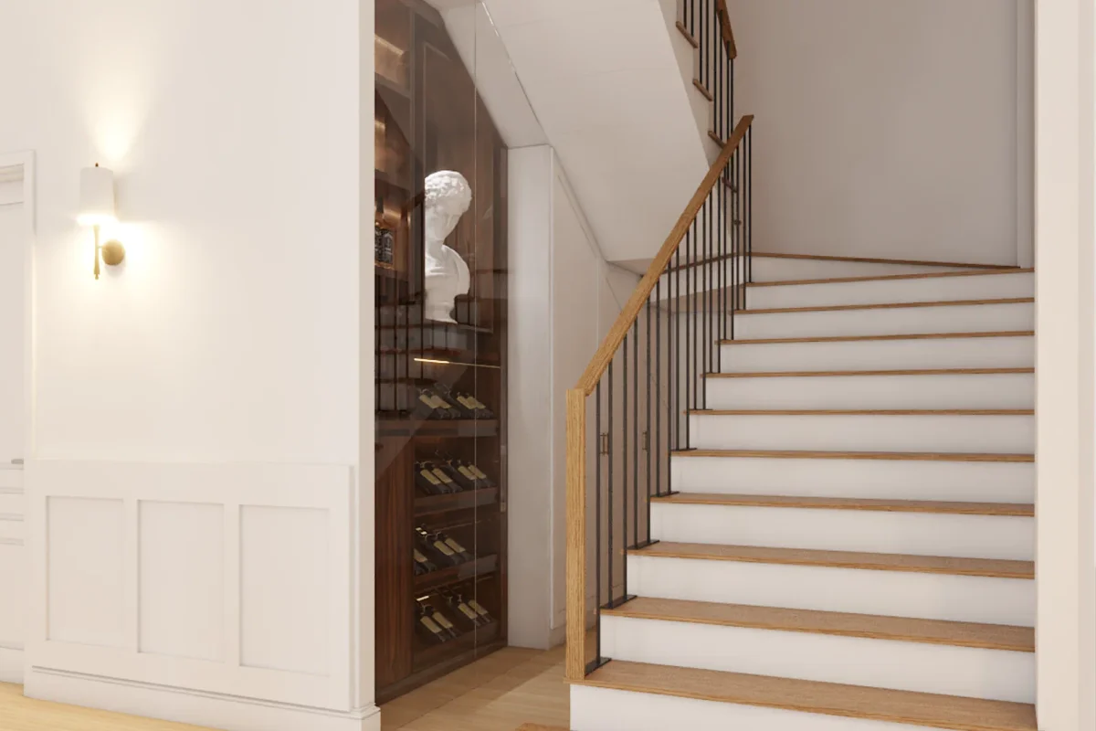 Under-stair wine cellar with arched dark-tinted glass door, walnut interior diamond wine racks holding bottles, white sculptural bust displayed inside, brass wall sconce on white wainscoted wall