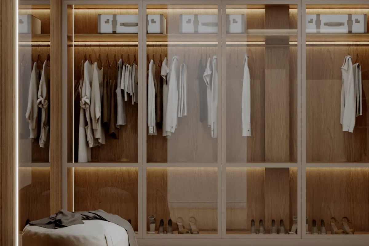 Oak glass-front wardrobe wall with full-height glass panels, LED-lit shelves, hanging cream and white clothing, organized shoe storage at base, and white storage boxes on top shelf