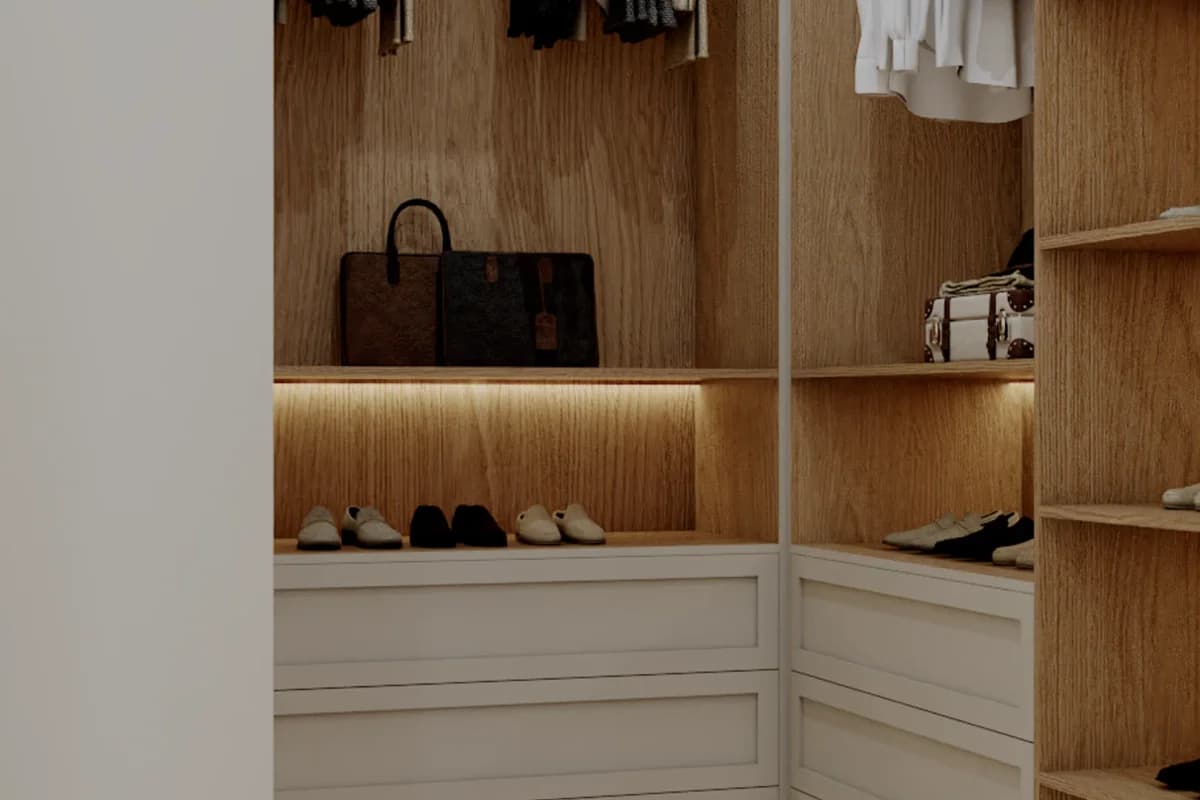 L-shaped walk-in closet with warm oak paneling, LED under-shelf lighting, open shoe shelf, and white shaker flat drawers at the base