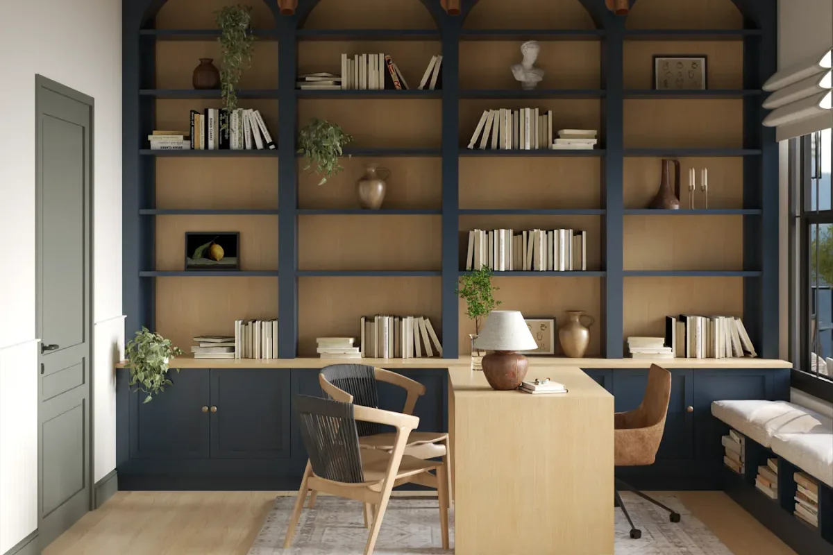 Navy blue floor-to-ceiling arched bookshelves with camel tan back panel, integrated oak floating desk, rattan chair, leather chair, and window seat in a home office