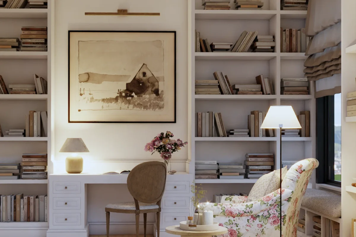 White floor-to-ceiling wraparound built-in bookshelves with integrated desk, white drawers, framed watercolor art, and floral reading chair in a cottage-style library