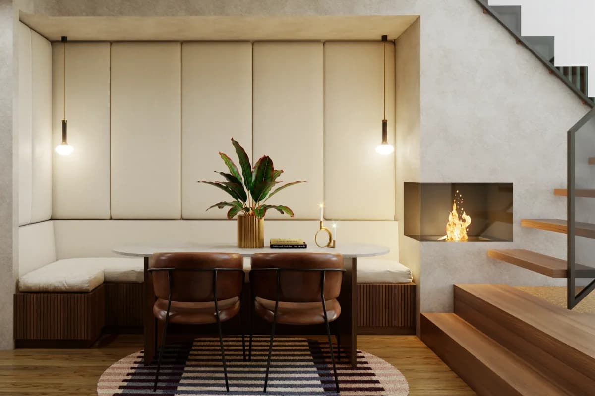 Contemporary dining nook with L-shaped cream upholstered banquette, round marble table, cognac dining chairs, fireplace, and brass pendant lights under open staircase