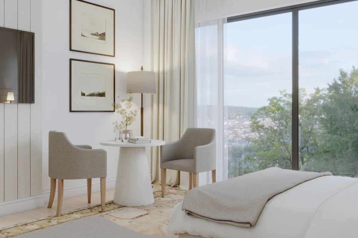 Minimalist bedroom sitting area with two gray armchairs, round white pedestal table, floor-to-ceiling window with sheer curtains, white panel wall, and framed landscape prints