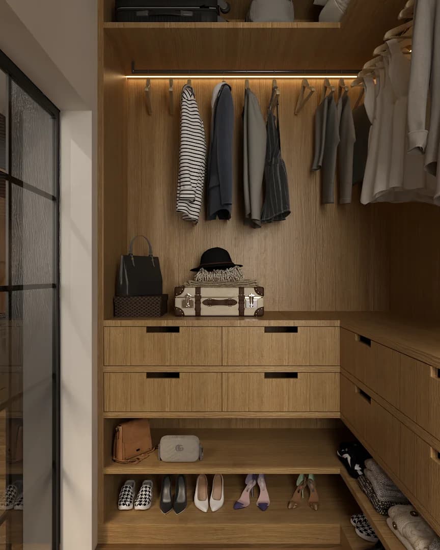 Walk-in closet with oak drawer tower, LED-lit hanging rod, open shelves holding leather bags and heels, and a vintage trunk on the counter. Design by Debora, an online interior design service.
