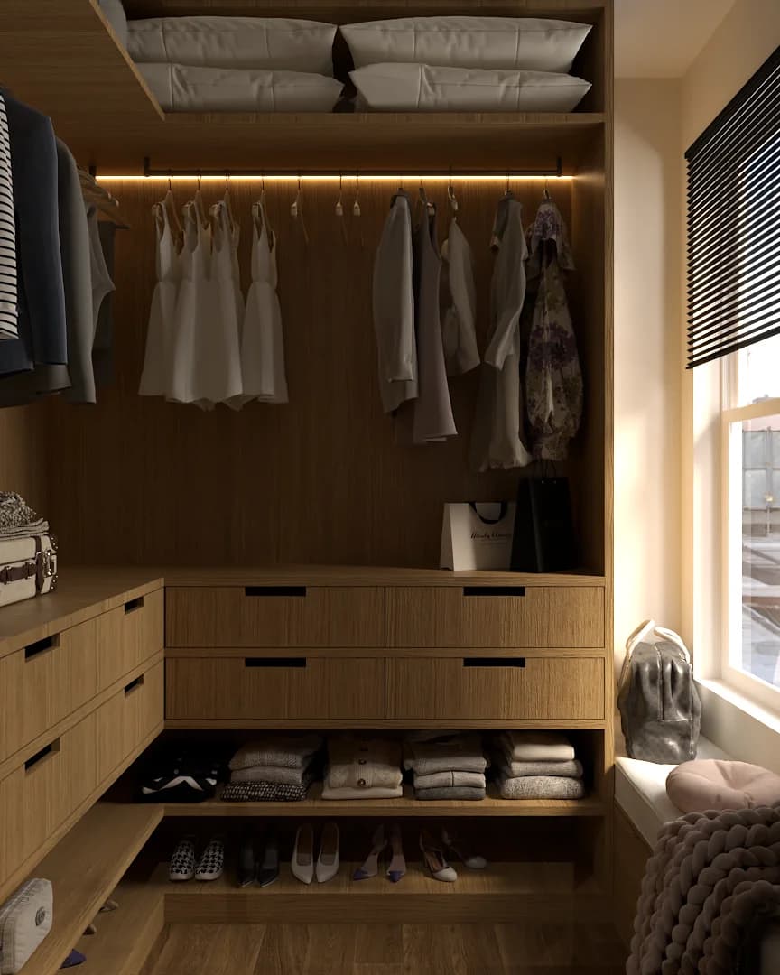 Oak walk-in closet with LED rail above white garments on hanging rod, four black-pull drawers below, folded sweaters and shoes on open shelves, and pillows stored on top shelf