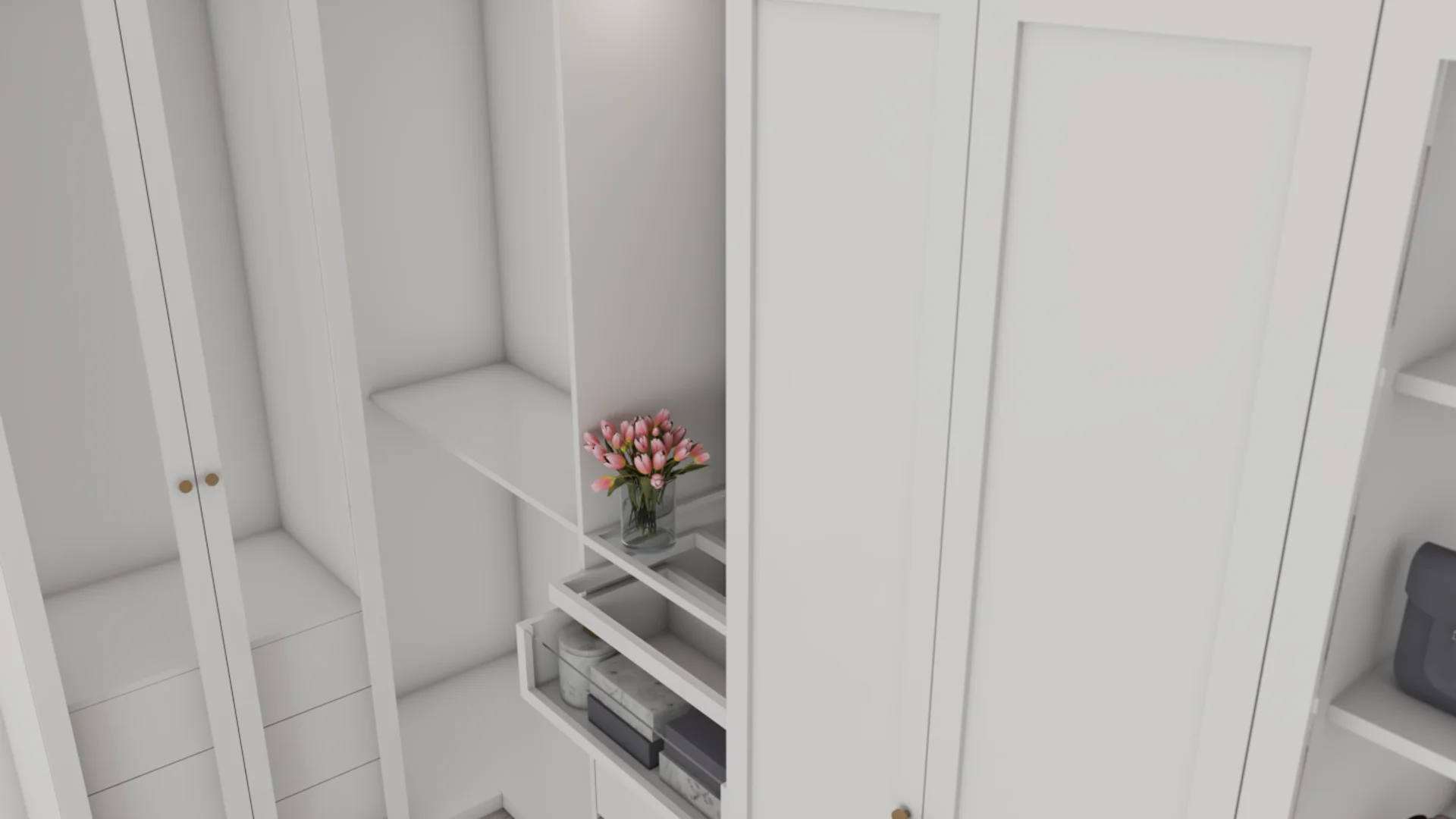 White shaker-style wardrobe with open pull-out shelves holding folded books and boxes, a glass vase of pink tulips on the middle shelf, brass knob hardware, and recessed overhead lighting.