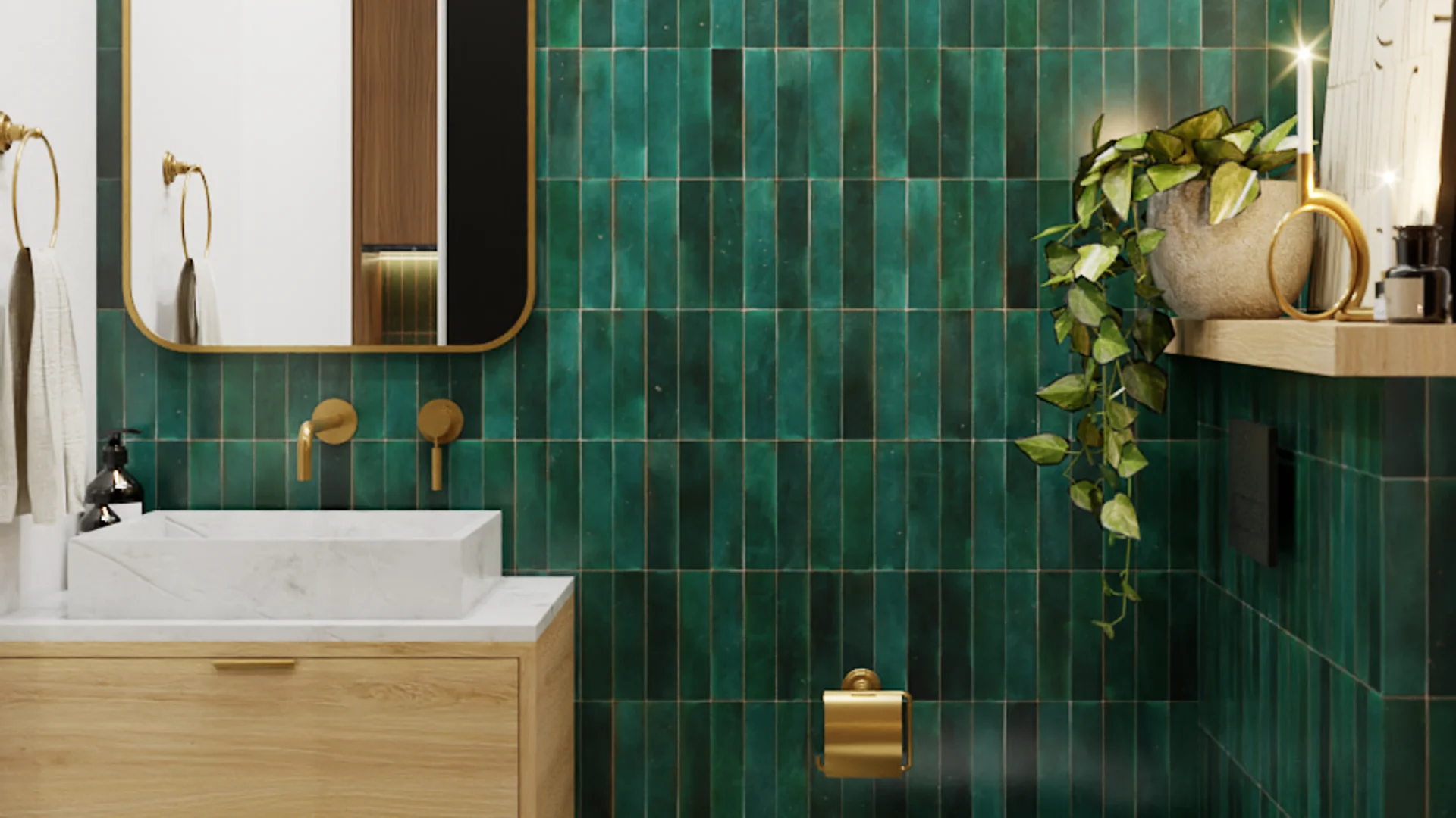 Bathroom with floor-to-ceiling emerald green zellige tile walls, wall-mounted brass faucet, white marble sink on oak floating vanity, rounded gold-framed mirror, trailing pothos plant on wood shelf, and gold accents