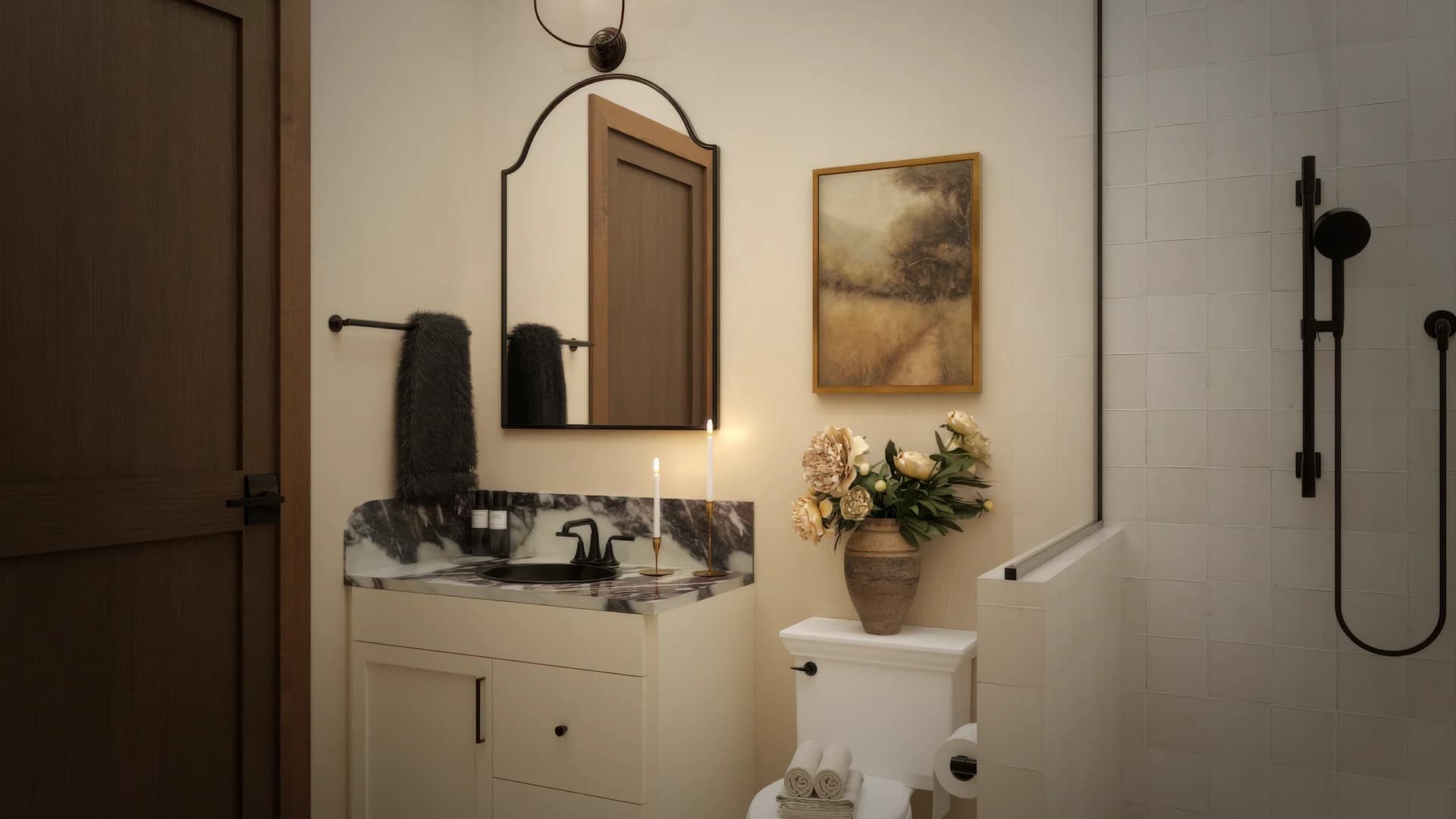 Wide guest bathroom view with cream vanity, arched mirror, landscape painting, walk-in shower with glass partition and rain showerhead, black fixtures, and mosaic tile floor