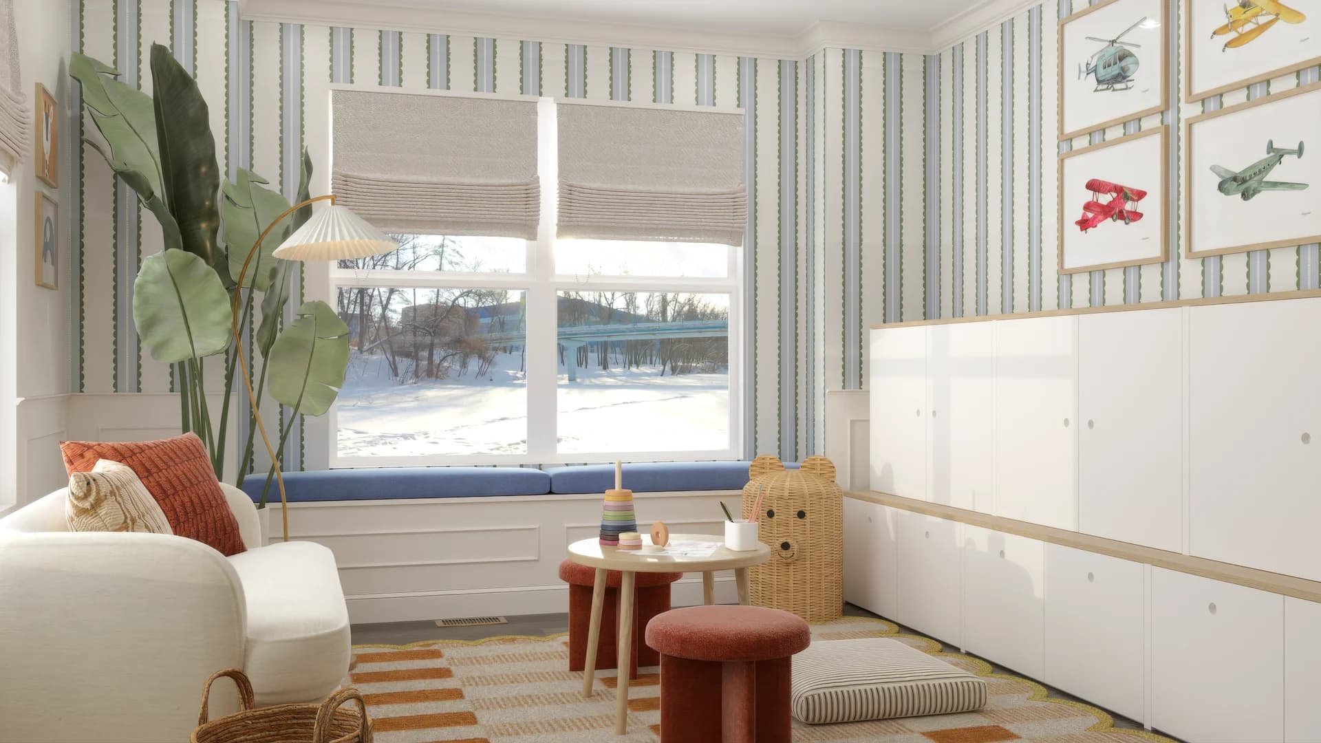 Kids playroom from second angle showing white built-in storage cabinets, framed vintage airplane prints on wall, striped blue wallpaper, wicker bear basket, round play table with terracotta stool, and tropical plant in corner.