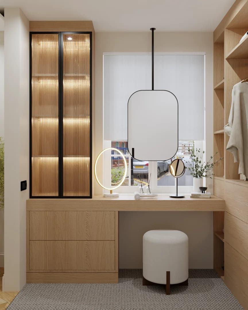 Built-in light oak dressing table with drawers, round white ottoman stool, black pendant mirror, circular LED vanity mirror, and ribbed glass cabinet with warm internal lighting beside a roller blind window