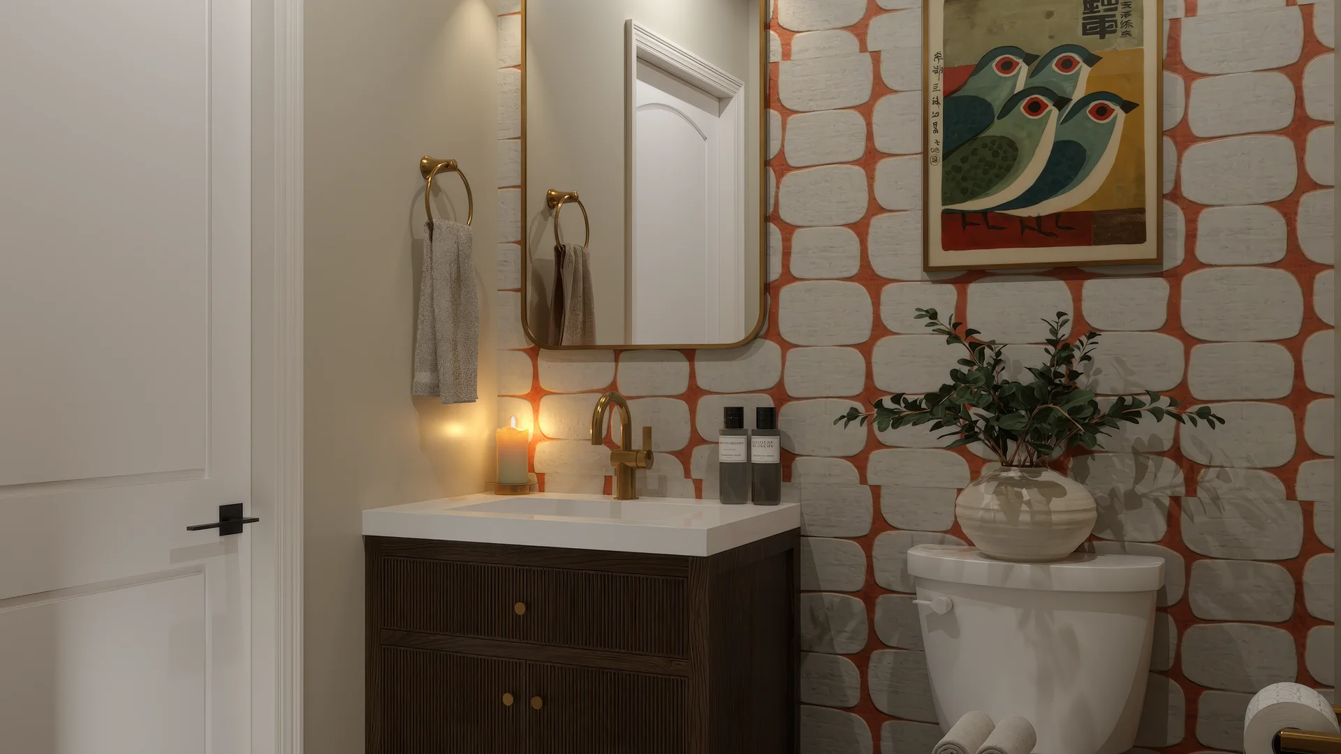 Close angle of powder room vanity with dark reeded espresso cabinet, brass round pulls, brass bridge faucet, white undermount sink, lit candle, skincare bottles, rectangular gold-framed mirror, brass towel ring, orange geometric block wallpaper, framed colorful bird print