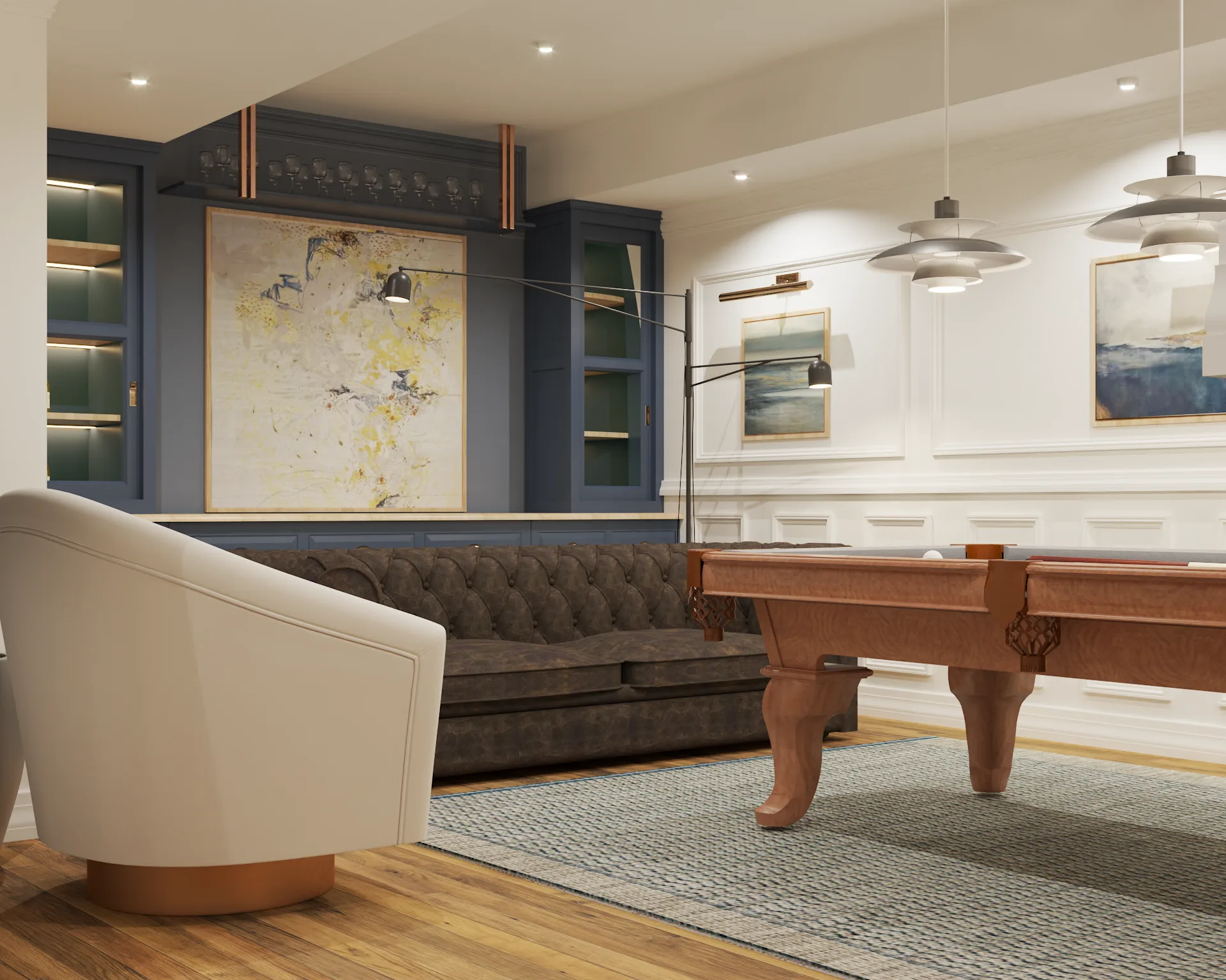 Billiards room with walnut pool table, navy built-in shelving, gray Chesterfield sofa, white barrel chair, and abstract art