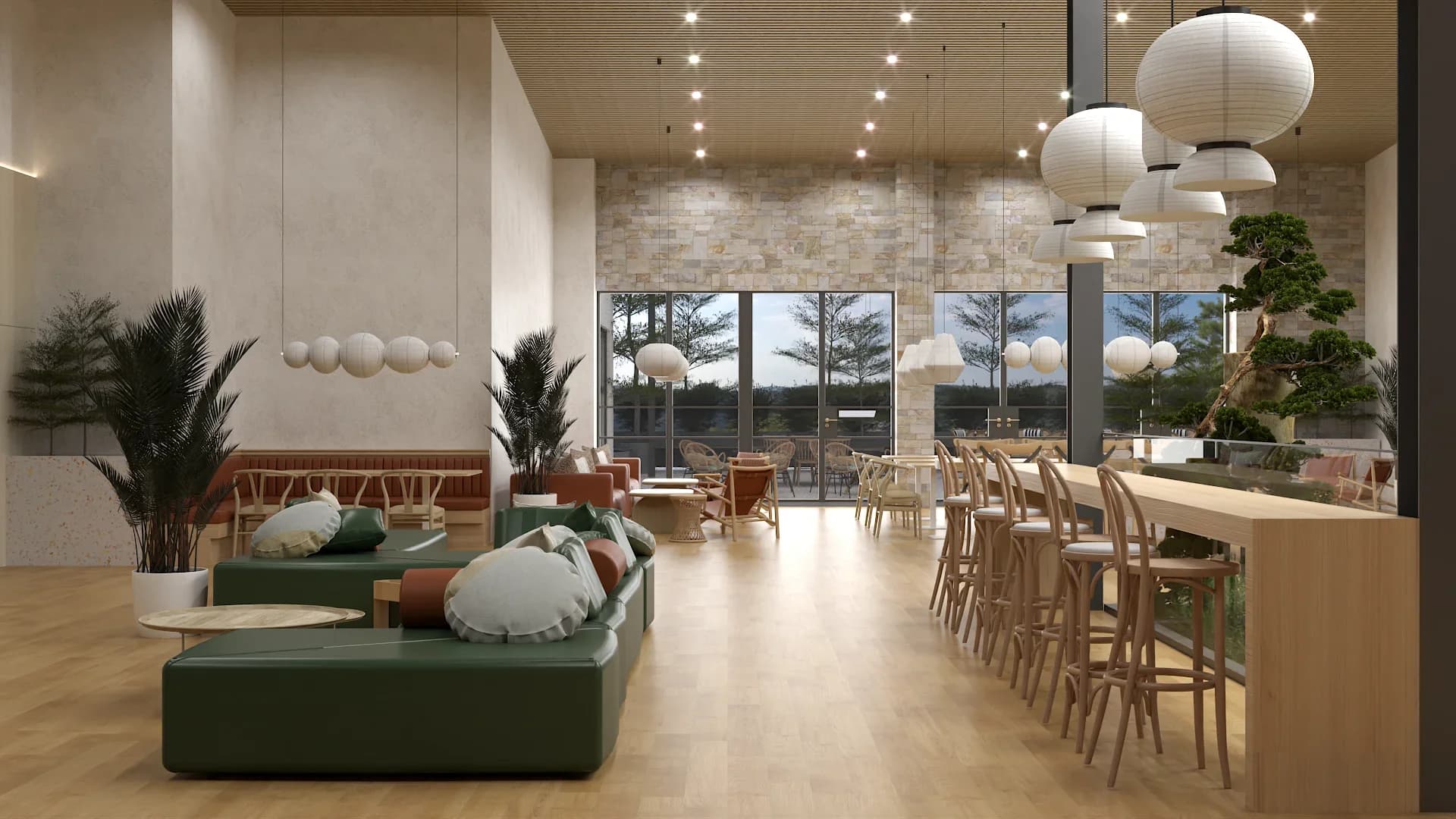 Wide view of a coastal restaurant featuring a green modular sofa with cushions, white paper lantern pendants, long wooden bar with stools, exposed stone feature wall with a bonsai tree, terracotta banquette seating in the background, and large sliding glass doors with tree-line views