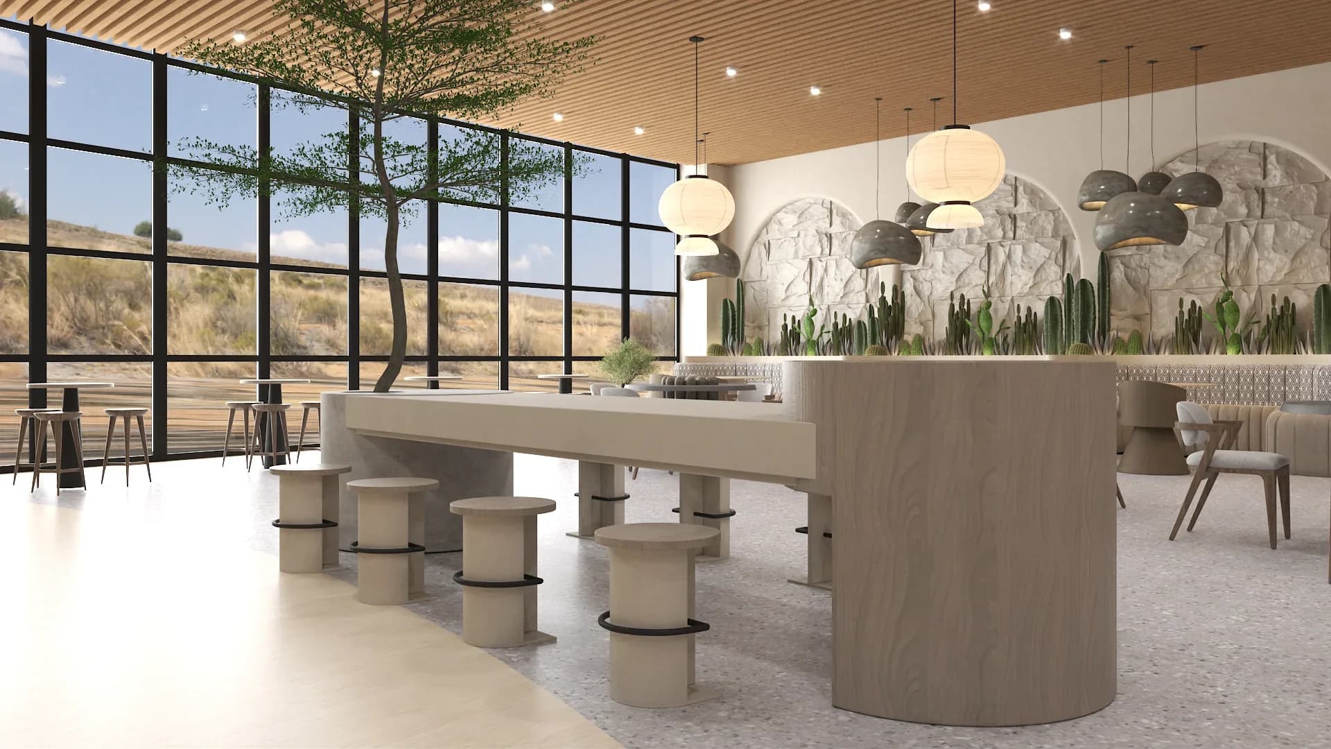 Central communal table with light concrete top and cylindrical wood-clad base surrounded by round upholstered stools, stone arches with cactus displays and paper lantern pendants in the background, black steel grid windows with desert views, a mature tree, and terrazzo flooring throughout