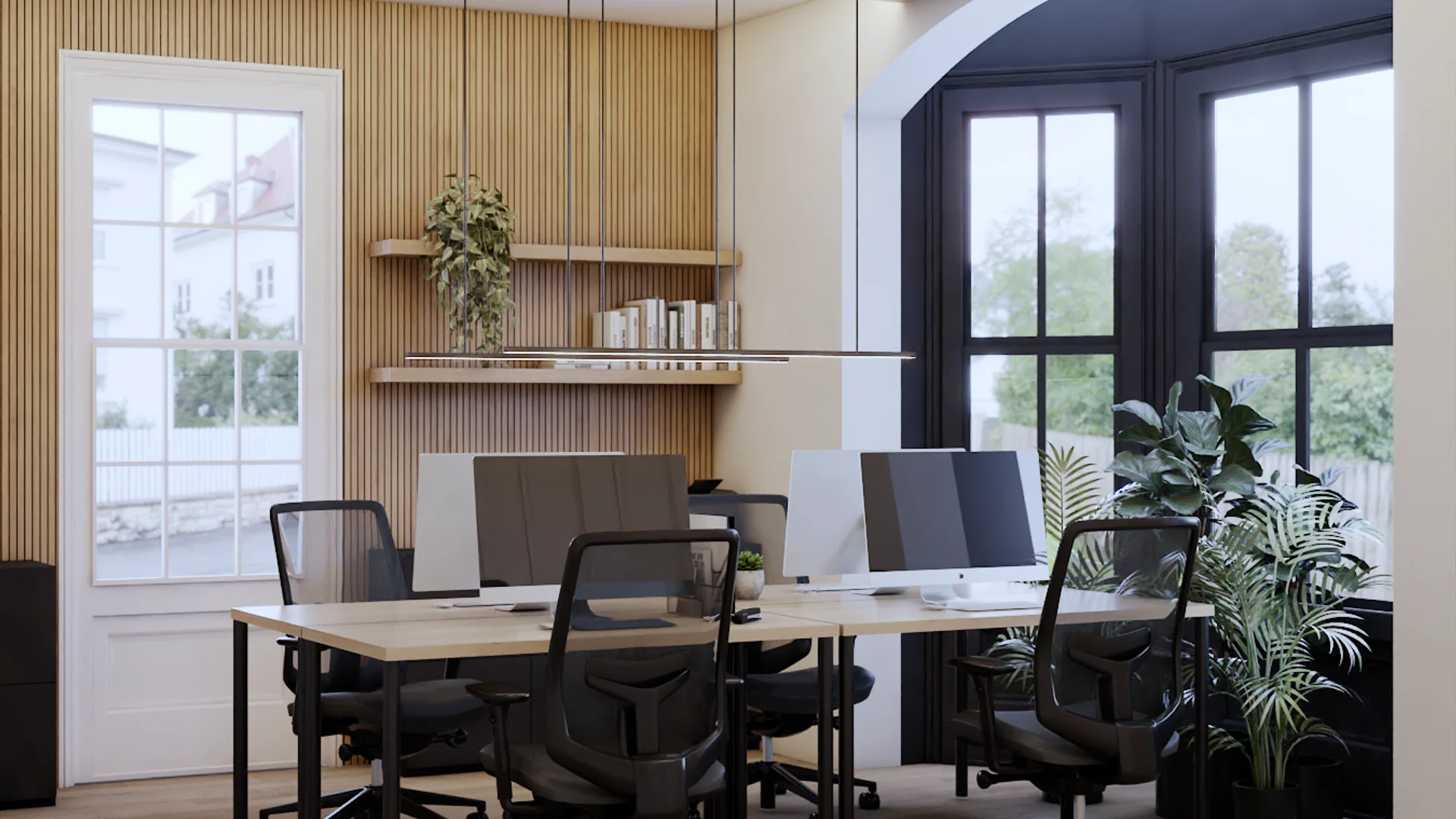 Office desk cluster of four workstations with monitors on light oak tables, black ergonomic chairs, oak wood slat accent wall with two floating shelves and a trailing plant, arched black-frame window on right with large palm