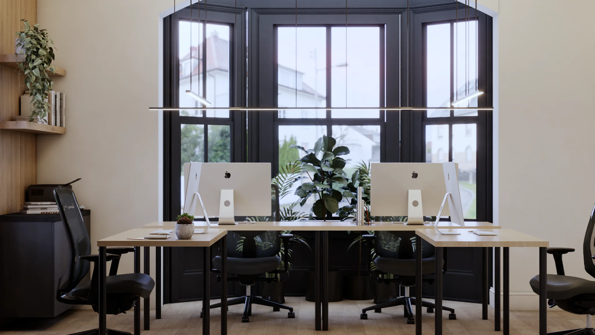 Front view of two iMac workstations on light oak desks facing a large black-framed bay window with arched top, linear pendant light overhead, black ergonomic chairs, potted fiddle leaf fig and palm plants, and floating shelves on the left wall