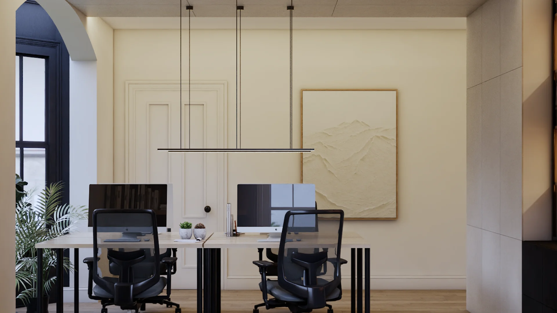 Two-person workstation with shared maple-top desk, black mesh ergonomic chairs, dual monitors, linear black pendant light overhead, cream paneled wall with moldings, textured beige canvas art in oak frame, arched dark window at left