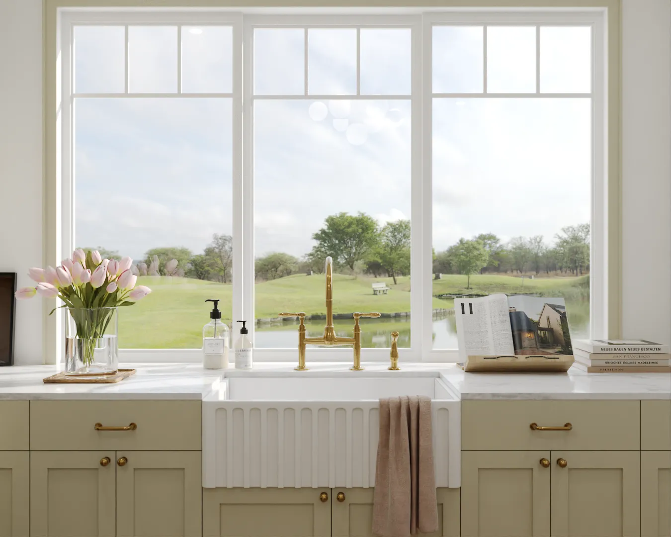 Bright farmhouse kitchen with a white farmhouse sink, marble countertops, fresh flowers, and a large window offering a scenic outdoor view.